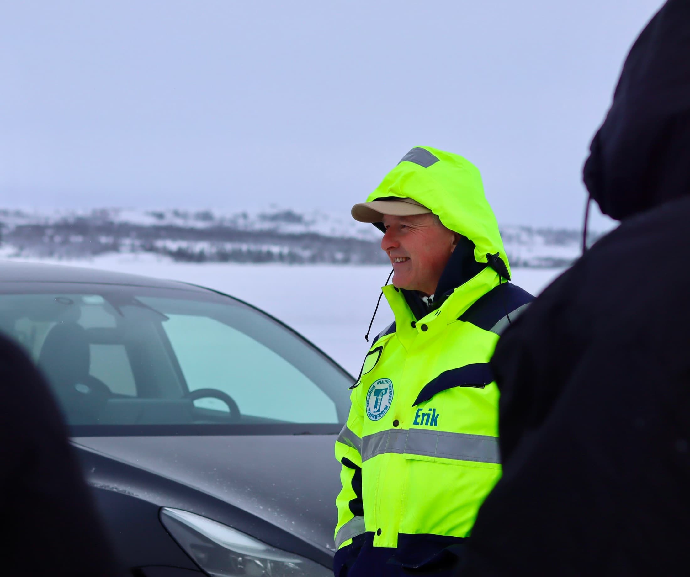 Kursholder i gul refleksjakke med Trafikkforum-logo orienterer kursdeltakere ved en bil på snødekt isbane
