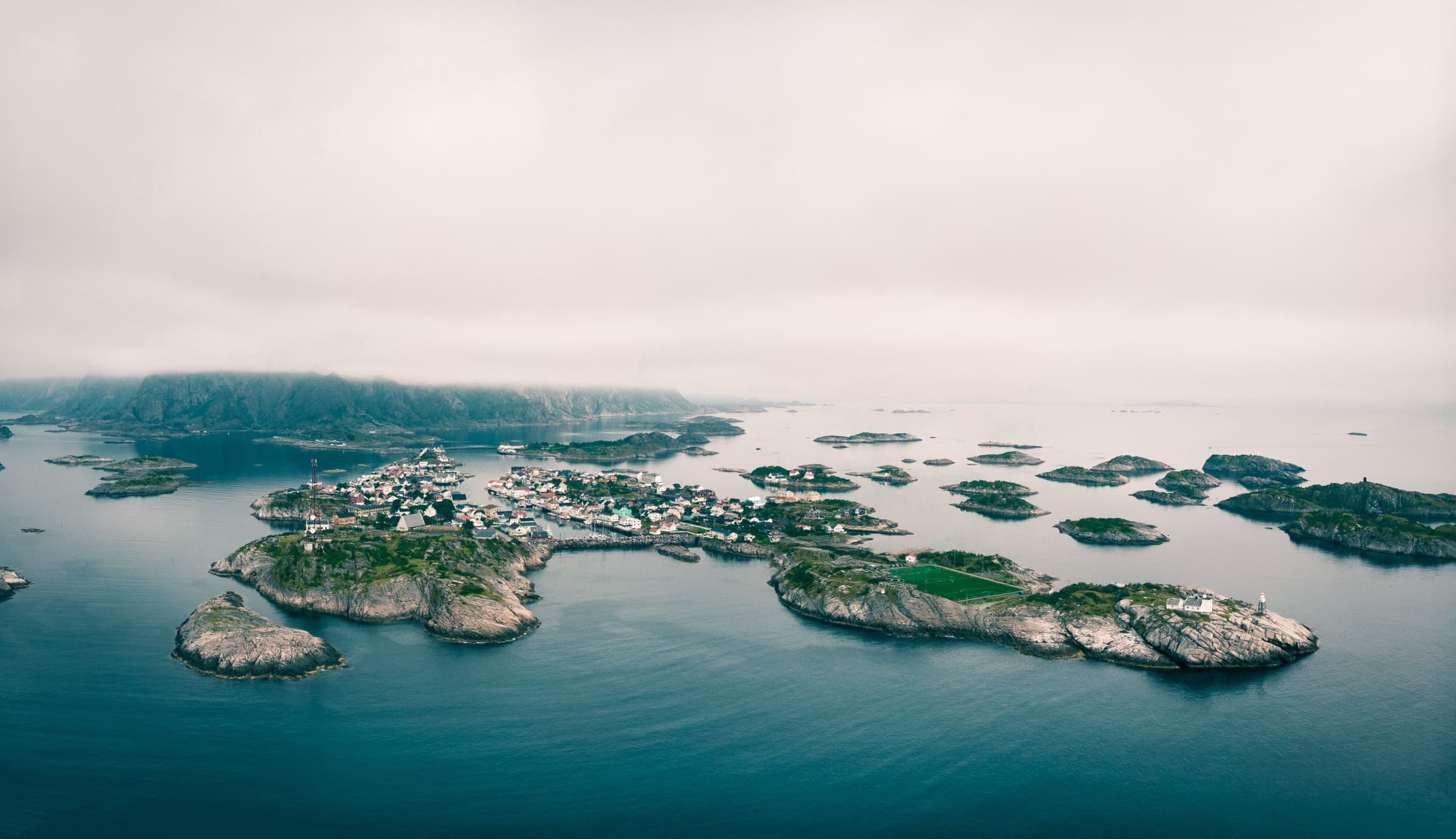 Luftfoto av Henningsvær i Lofoten – et norsk øysamfunn med hus og veier omgitt av hav og fjell.
